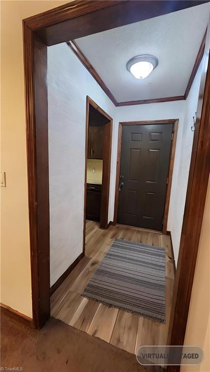 doorway to outside with crown molding, light wood-type flooring, and baseboards