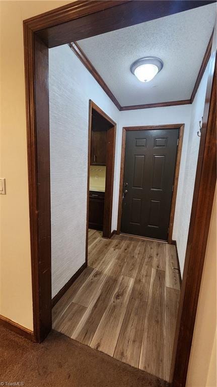 hallway with a textured ceiling, light wood-style flooring, baseboards, and ornamental molding