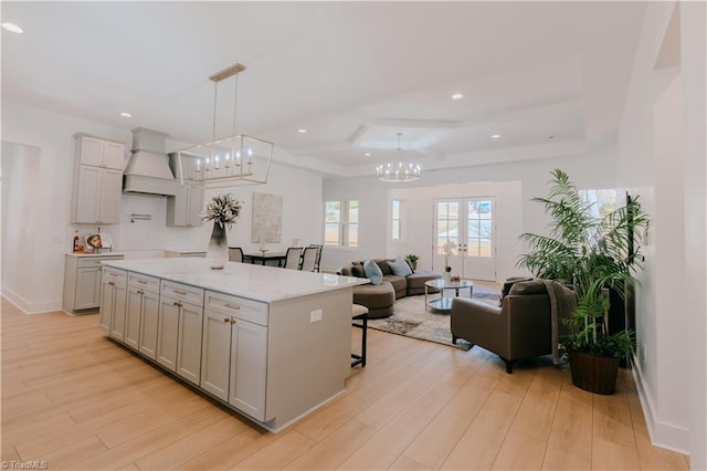 kitchen with light stone countertops, an inviting chandelier, premium range hood, light hardwood / wood-style floors, and decorative light fixtures