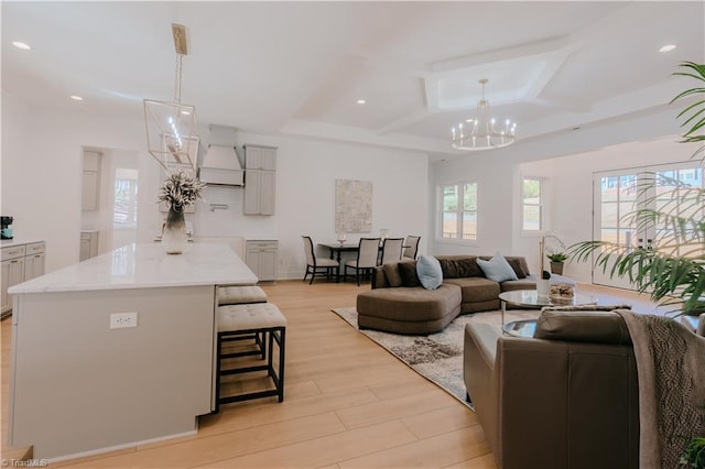 living room featuring light hardwood / wood-style flooring, a notable chandelier, a healthy amount of sunlight, and coffered ceiling