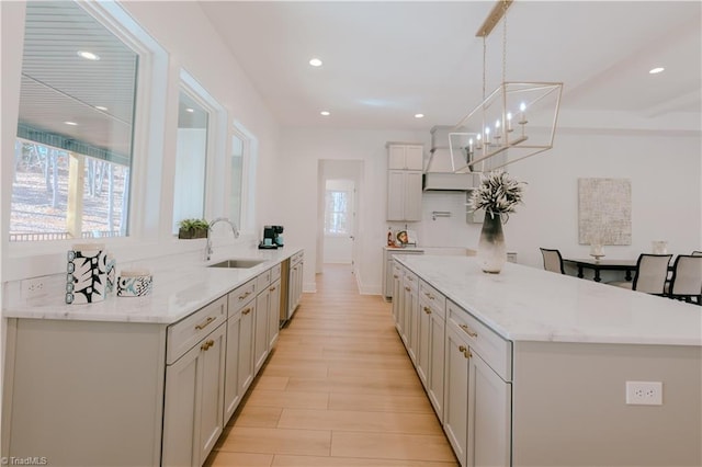 kitchen with light stone counters, custom exhaust hood, sink, decorative light fixtures, and light hardwood / wood-style flooring