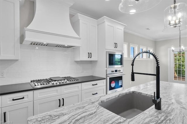 kitchen with premium range hood, a sink, white cabinets, appliances with stainless steel finishes, and an inviting chandelier