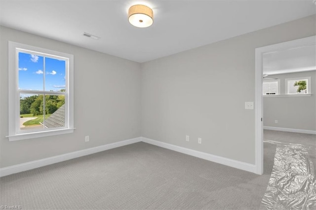 spare room featuring carpet floors, a healthy amount of sunlight, visible vents, and baseboards