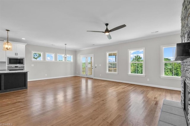 unfurnished living room with crown molding, a fireplace, light wood-style floors, baseboards, and ceiling fan with notable chandelier