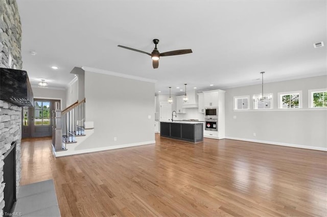 unfurnished living room with stairway, crown molding, a stone fireplace, light wood-type flooring, and a sink