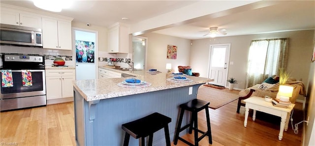 kitchen with white cabinetry, a kitchen breakfast bar, decorative backsplash, light hardwood / wood-style floors, and stainless steel appliances