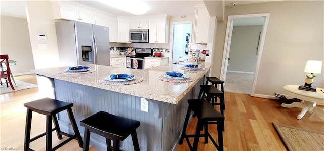 kitchen featuring light stone countertops, white cabinetry, appliances with stainless steel finishes, and a kitchen breakfast bar