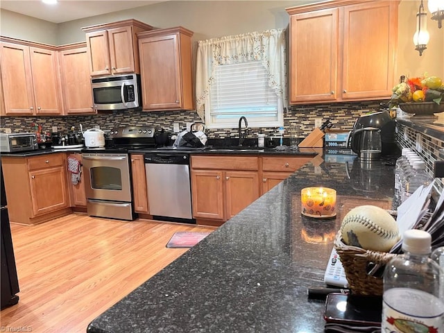 kitchen featuring pendant lighting, sink, light hardwood / wood-style flooring, decorative backsplash, and appliances with stainless steel finishes