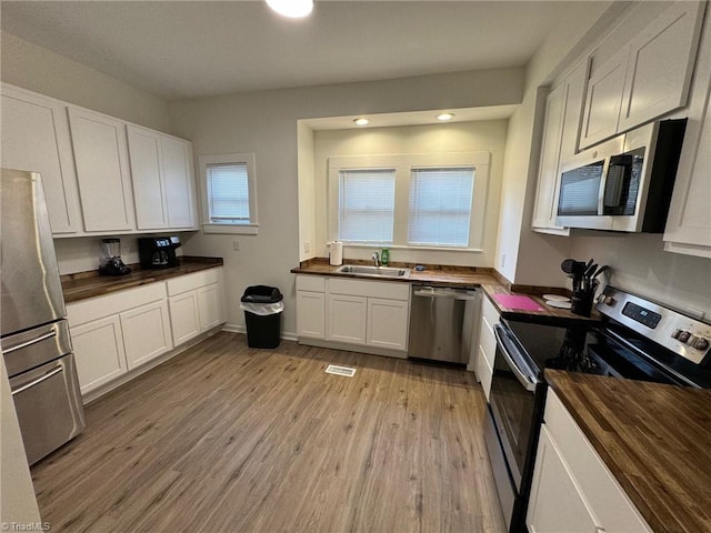 kitchen with wooden counters, light wood-type flooring, stainless steel appliances, sink, and white cabinetry