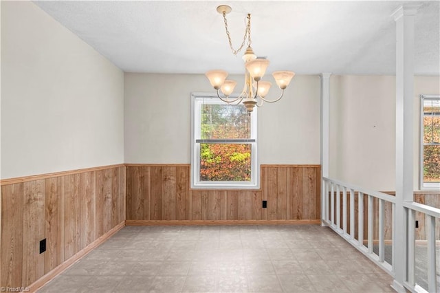 empty room featuring wood walls, a chandelier, and a healthy amount of sunlight