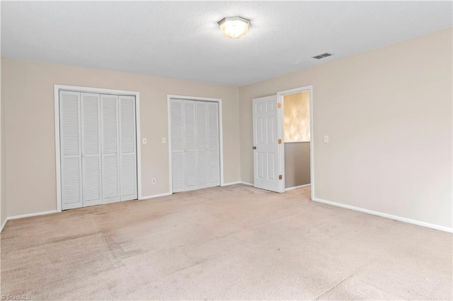 unfurnished bedroom featuring multiple closets and light carpet