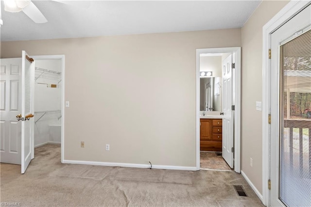 bedroom with ceiling fan, ensuite bath, light carpet, and a spacious closet