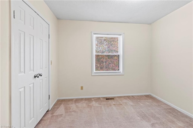 unfurnished bedroom with light colored carpet, a textured ceiling, and a closet