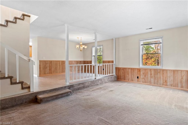 carpeted empty room with plenty of natural light, wooden walls, and a notable chandelier