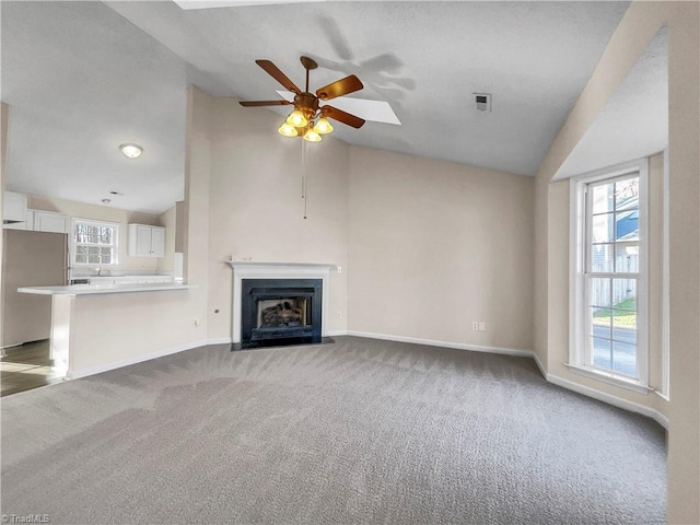 unfurnished living room with lofted ceiling, a fireplace with flush hearth, ceiling fan, and carpet flooring