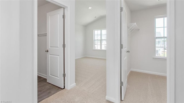 hallway with light carpet, vaulted ceiling, and a wealth of natural light