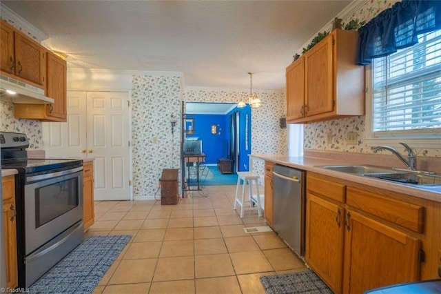 kitchen with wallpapered walls, light tile patterned floors, stainless steel appliances, under cabinet range hood, and a sink