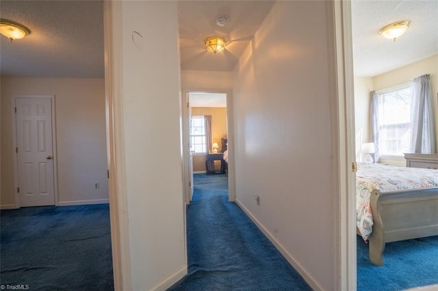 hall with dark carpet, a textured ceiling, and baseboards