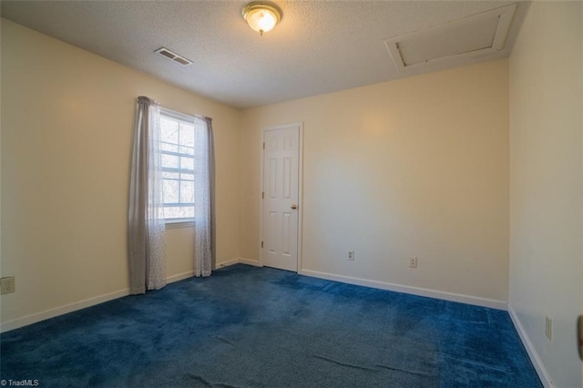 unfurnished room with attic access, baseboards, visible vents, a textured ceiling, and dark carpet