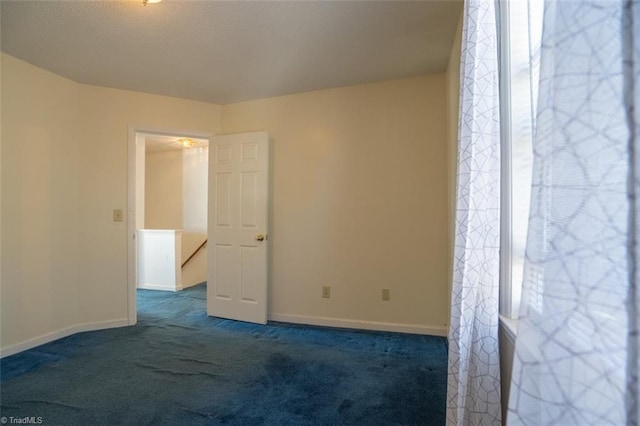 spare room featuring dark carpet and baseboards