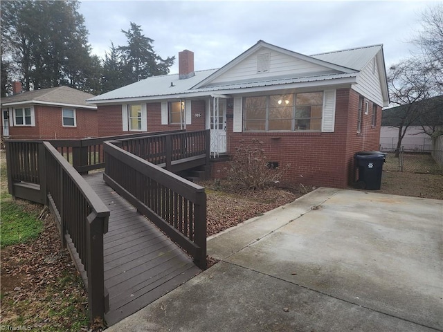 view of front of property with a deck, a chimney, metal roof, and brick siding