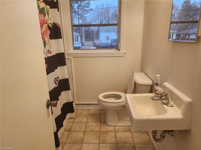 bathroom featuring a shower with shower curtain, toilet, a baseboard radiator, stone tile flooring, and a sink