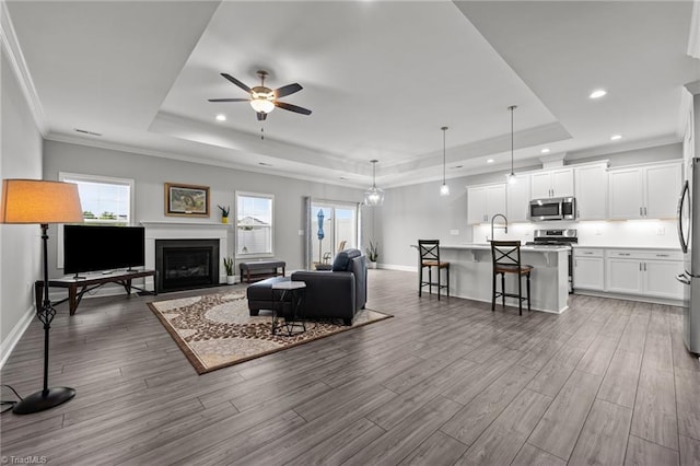 6624 Knob Creek Dr, Whitsett, NC 27377 - living room with a tray ceiling, recessed lighting, wood finished floors, baseboards, and ornamental molding
