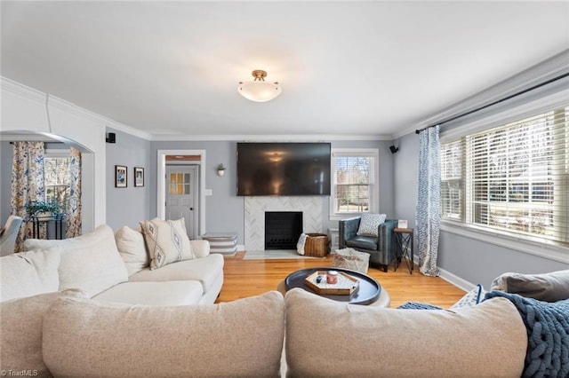 living room featuring a high end fireplace, crown molding, baseboards, light wood-style floors, and arched walkways