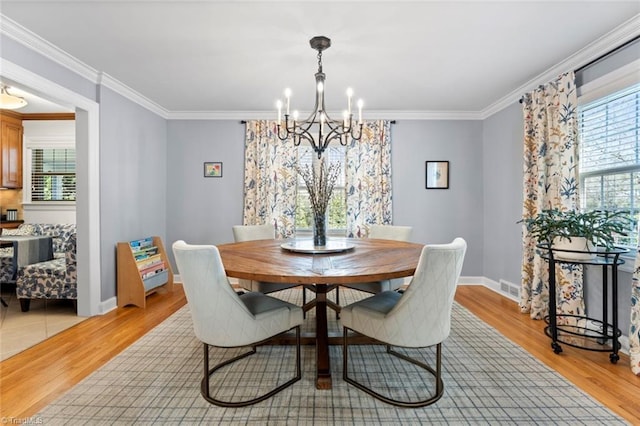 dining area with baseboards, visible vents, light wood-style flooring, ornamental molding, and a chandelier