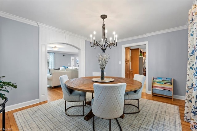 dining room with baseboards, arched walkways, ornamental molding, and light wood finished floors