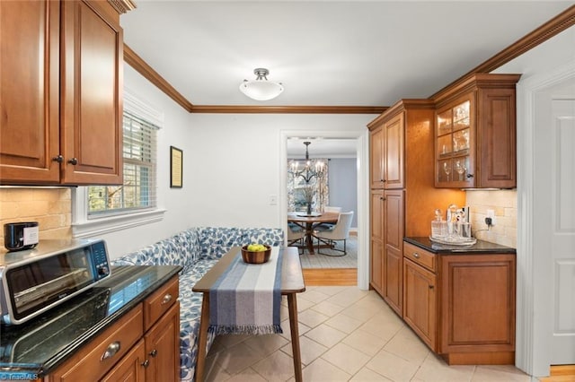 kitchen with brown cabinets, backsplash, dark stone counters, crown molding, and glass insert cabinets