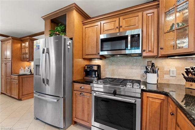 kitchen with brown cabinets, dark stone counters, stainless steel appliances, glass insert cabinets, and tasteful backsplash