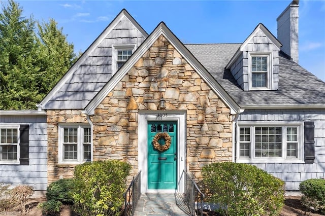 doorway to property with stone siding, a chimney, and a shingled roof