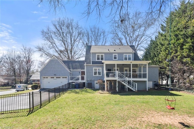 rear view of house with fence, driveway, stairs, a garage, and a lawn