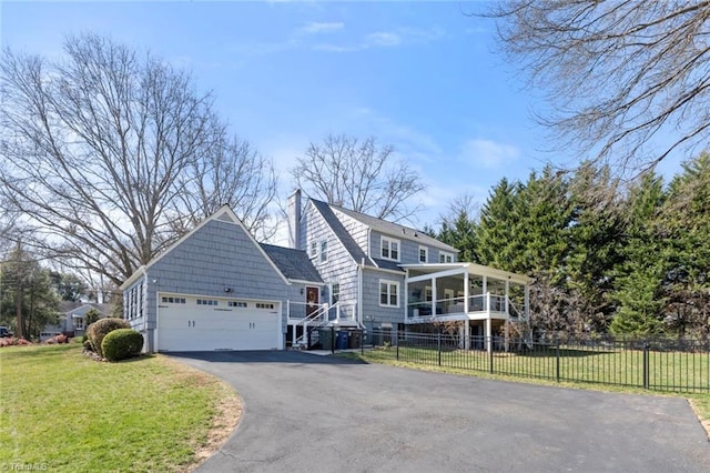 view of side of property featuring fence, an attached garage, a sunroom, aphalt driveway, and a lawn