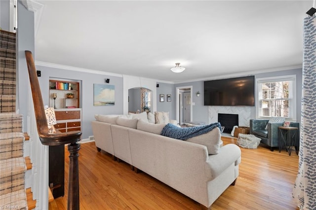 living room featuring stairway, arched walkways, ornamental molding, and light wood finished floors