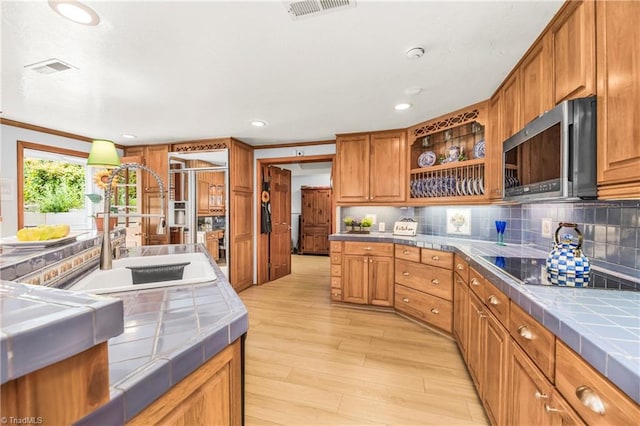 kitchen featuring black electric stovetop, tasteful backsplash, crown molding, light wood-type flooring, and tile countertops