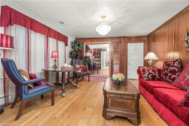 living room featuring wood walls, a notable chandelier, light hardwood / wood-style flooring, and crown molding