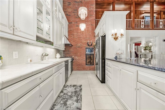 kitchen with stainless steel appliances, white cabinets, hanging light fixtures, light tile patterned flooring, and brick wall