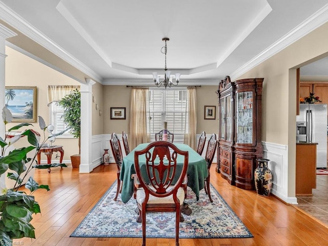 dining room featuring a chandelier, a raised ceiling, decorative columns, and light hardwood / wood-style flooring