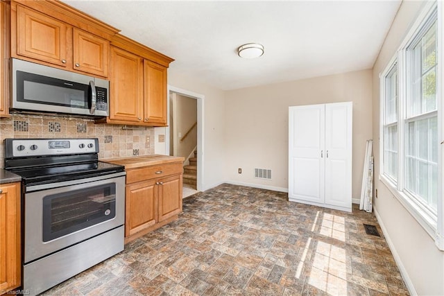 kitchen featuring visible vents, baseboards, stainless steel appliances, decorative backsplash, and stone finish flooring