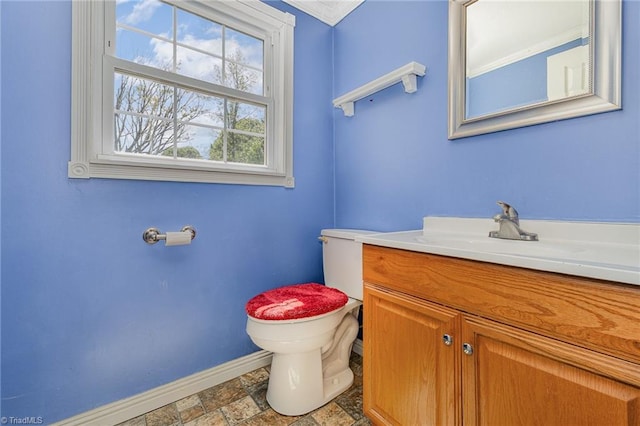 half bathroom with toilet, stone finish floor, vanity, and baseboards