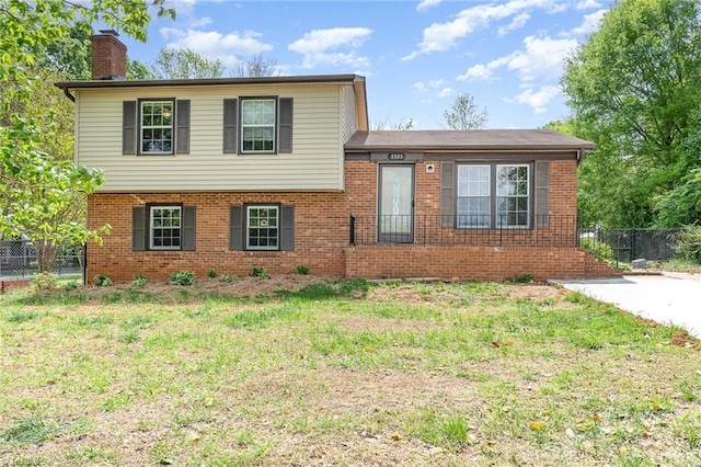tri-level home featuring brick siding, fence, and a front lawn