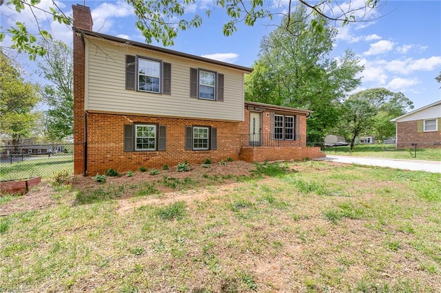 split level home with brick siding, a front lawn, fence, and a chimney