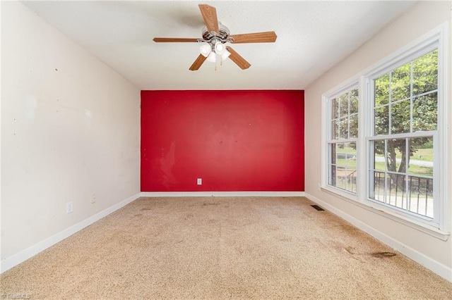 carpeted spare room featuring visible vents, ceiling fan, and baseboards