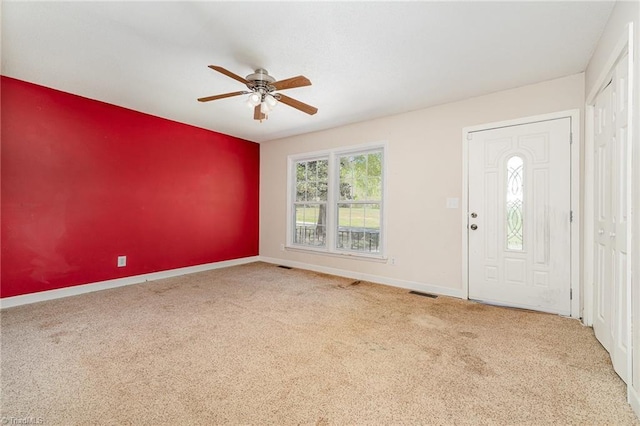 carpeted entryway with visible vents, ceiling fan, an accent wall, and baseboards