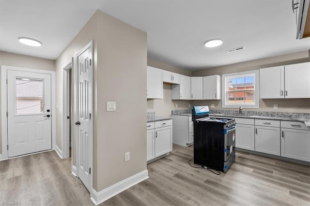 kitchen featuring a sink, light wood-style flooring, gas range oven, and white cabinets