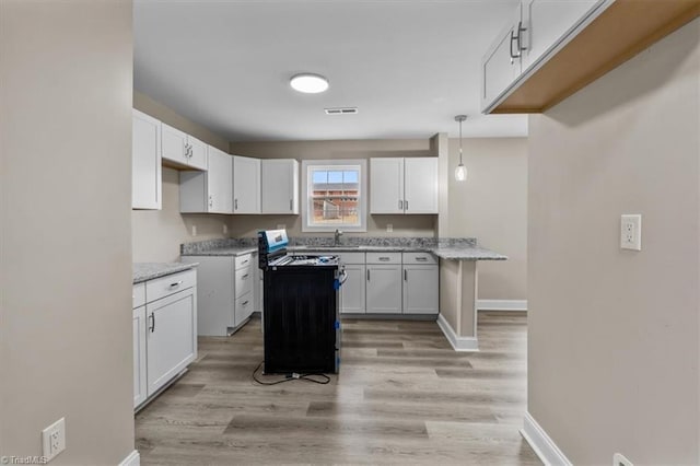 kitchen with gas stove, baseboards, light wood finished floors, a sink, and white cabinetry