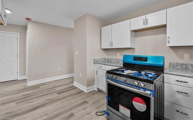 kitchen with light wood-style flooring, light stone counters, stainless steel range with gas cooktop, white cabinets, and baseboards