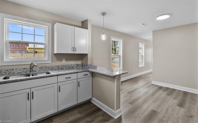 kitchen featuring visible vents, baseboards, a peninsula, wood finished floors, and a sink